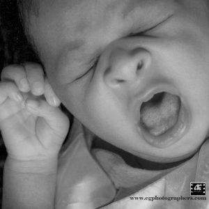 A black and white portrait of a yawning new born baby