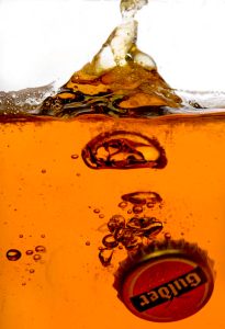 Beer bottle cap submerged in liquid with splash and bubbles in creative product photography