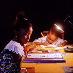 Two children studying and doing homework at night under a table lamp in a dark setting, education photography in Nigeria