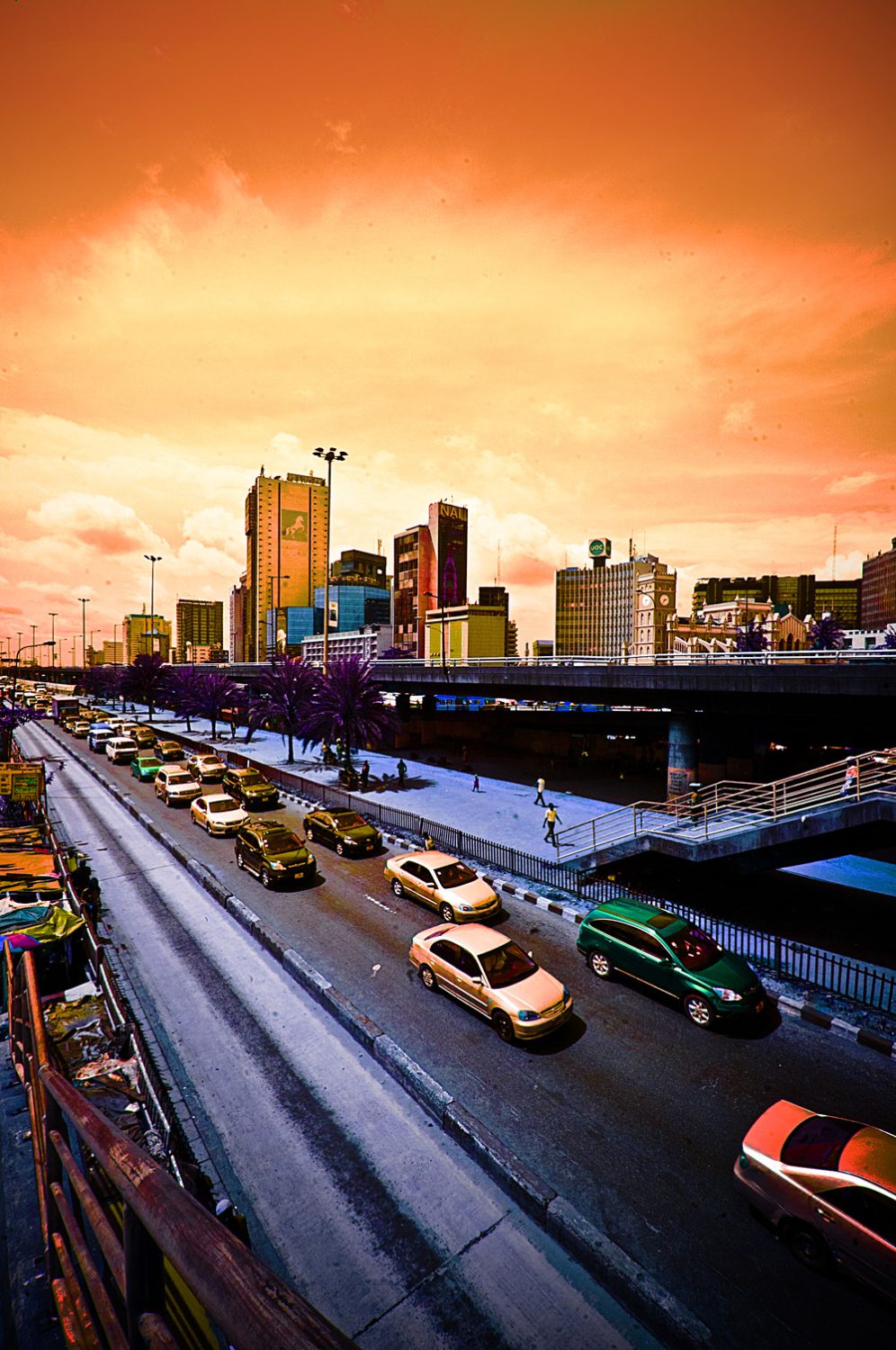 Traffic on a busy Lagos road with city skyline and bridge under a vibrant sunset sky