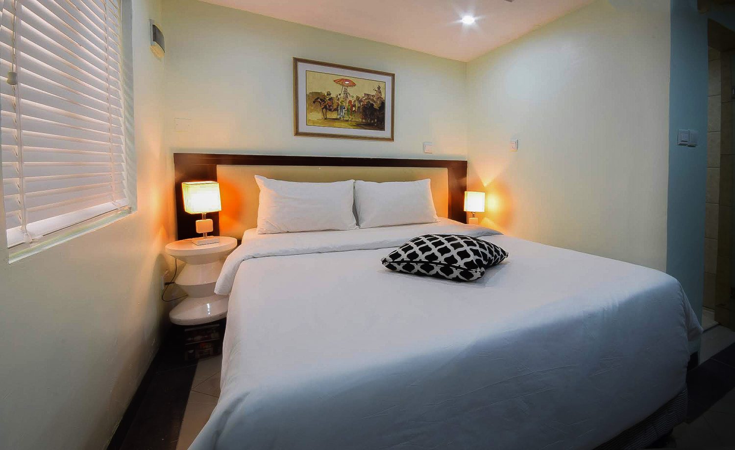 A clean and modern hotel bedroom featuring a king-size bed, soft lighting, and a comfortable, inviting atmosphere.