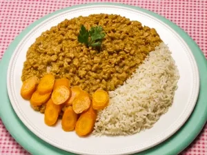 Plate of white rice served with Nigerian stew and sliced carrots on a patterned tablecloth