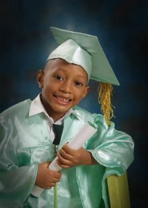 Young child wearing graduation gown and cap holding certificate during school graduation portrait session